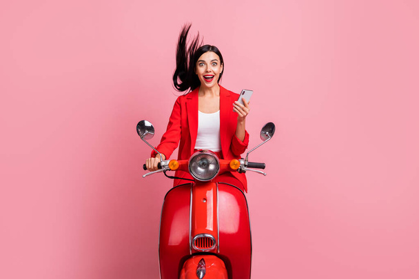 Photo of young excited girl happy positive smile amazed surprised browse cellphone ride bike isolated over pink color background - Foto, Imagem