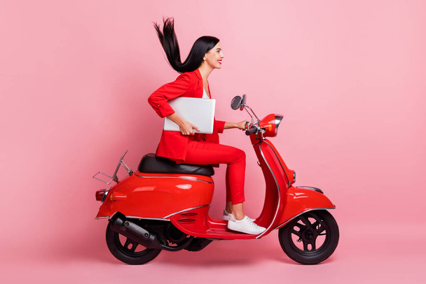 Full size profile side photo of young smiling beautiful woman riding moped with laptop isolated on pink color background - Φωτογραφία, εικόνα
