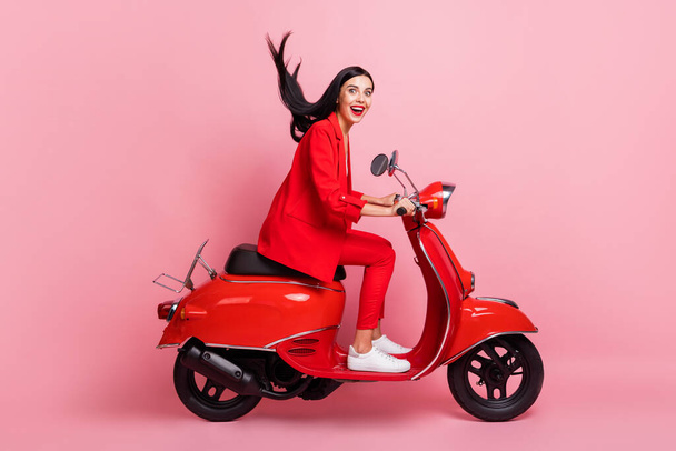 Full size profile side photo of young crazy excited smiling girl riding moped fast extreme isolated on pink color background - 写真・画像
