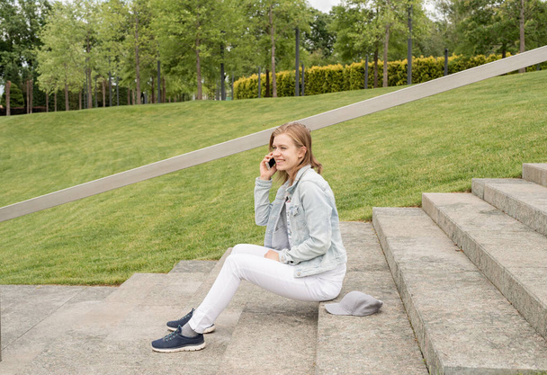 Woman in jeans clothes texting on her mobile phone, sitting on the stairs in the park - Fotó, kép