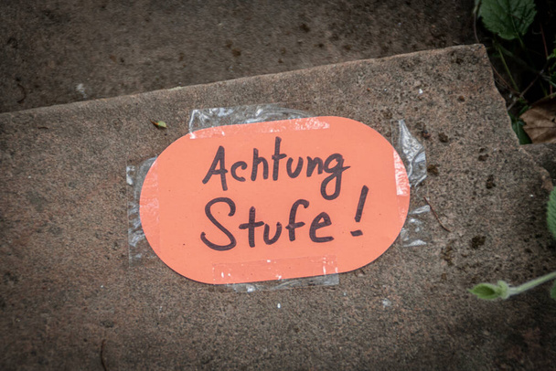 Aviso de papel pegado en el escalón de una escalera de arenisca exterior con la inscripción alemana "Vorsicht Stufe" que significa paso de precaución. - Foto, imagen