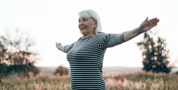 Happy Caucasian woman standing in meadow and show hand up at sunrise, enjoying the sun. Tourism, traveling and healthy lifestyle concept. - Φωτογραφία, εικόνα