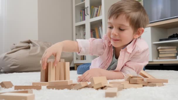 Kleine jongen bouwhuis van speelgoed houten blokken op de vloer in de woonkamer. Concept van kinderopvoeding en spelletjes thuis - Video