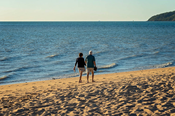 Cabo Gloucester, Queensland, Australia - Junio 2021: Pareja caminando por la playa sosteniendo sus zapatos disfrutando de sus vacaciones al aire libre junto al mar - Foto, Imagen