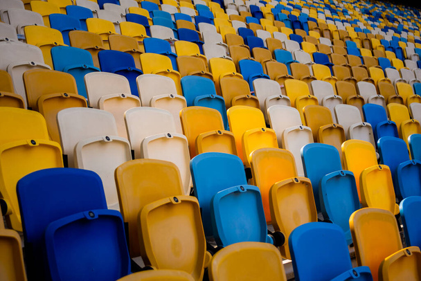 Empty rows of seats in a football olympic stadium with yellow and blue benches - Zdjęcie, obraz