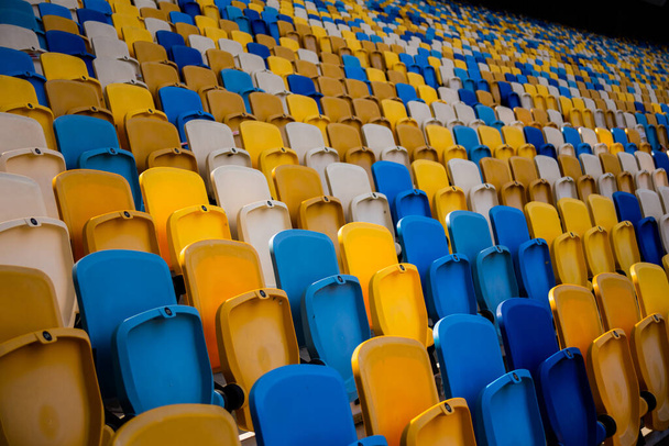 Пустые ряды мест на футбольном олимпийском стадионе с желтыми и синими скамейками - Фото, изображение