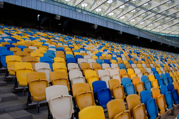 Filas vacías de asientos en un estadio olímpico de fútbol con bancos amarillos y azules - Foto, imagen