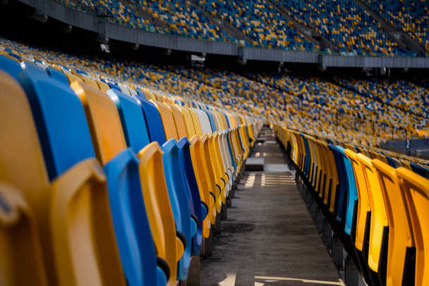 Filas vacías de asientos en un estadio olímpico de fútbol con bancos amarillos y azules - Foto, imagen