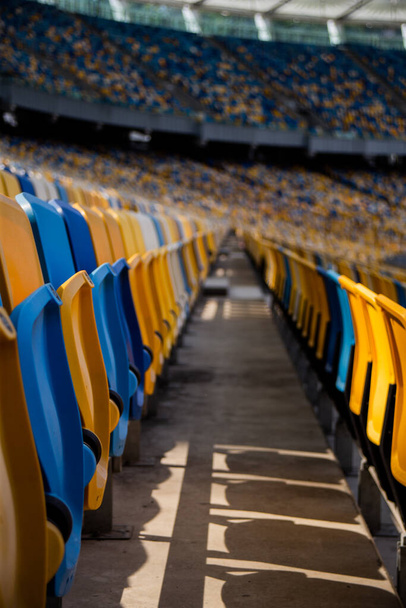 Empty rows of seats in a football olympic stadium with yellow and blue benches - Foto, Imagen