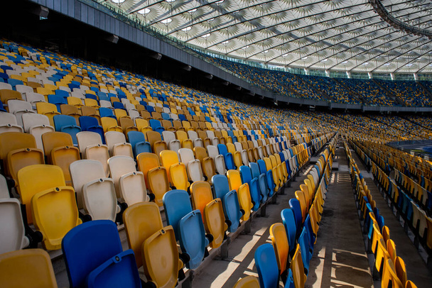 Κενές σειρές καθισμάτων σε ποδοσφαιρικό ολυμπιακό στάδιο με κίτρινα και μπλε παγκάκια - Φωτογραφία, εικόνα