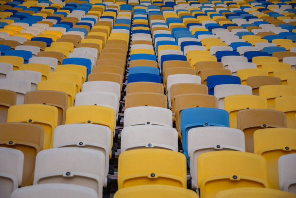 Puste rzędy miejsc na stadionie piłkarskim z żółtymi i niebieskimi ławkami - Zdjęcie, obraz
