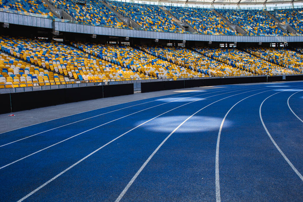 Lege blauwe hardloopbaan bij het Olympisch stadion tegen de achtergrond van lege tribunes - Foto, afbeelding