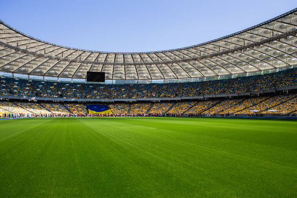 Bandera de Ucrania y multitud de personas en el estadio olímpico de fútbol con bancos amarillos y azules - Foto, imagen