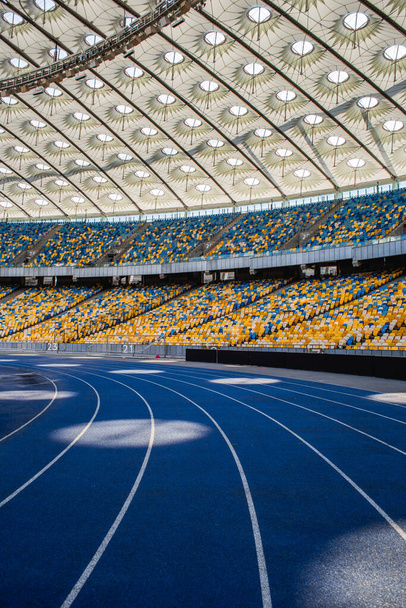 Lege blauwe hardloopbaan bij het Olympisch stadion tegen de achtergrond van lege tribunes - Foto, afbeelding
