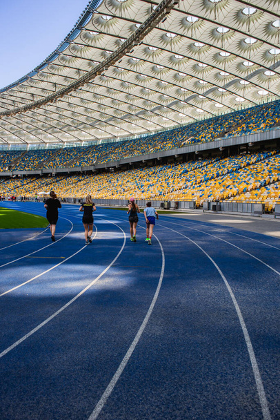 Biegi sportowców na pustym niebieskim torze do biegania na stadionie olimpijskim na tle pustych trybun - Zdjęcie, obraz