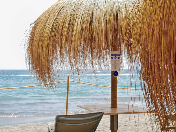 Meditterraner chill out place under a parasol made of bast, right on the water's edge of the Atlantic in the sand in Tenerife south in Adeje. Um idílio de arrepios com água ligeiramente azul e sem pessoas. - Foto, Imagem