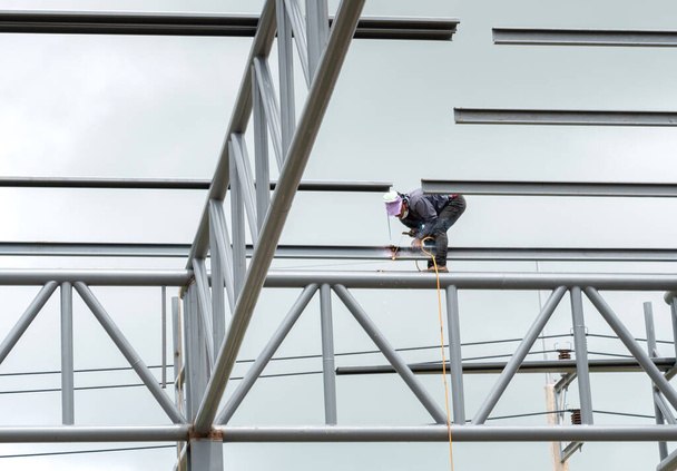Průmyslový pracovník se svařovací ocelí pro stavbu střešní konstrukce továrny. - Fotografie, Obrázek