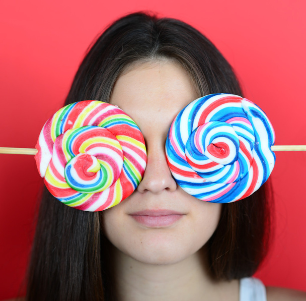 Portrait of woman covering eyes with lollipops against red backg - 写真・画像