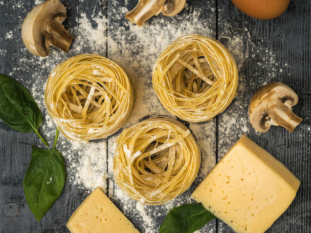 Cheese with rolled pasta and mushrooms on a wooden table. Ingredients for making pasta. - Photo, Image