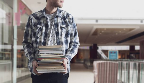 un estudiante sosteniendo pila de libros, llevar libros de texto de papel pesado, concepto de motivación - Foto, imagen