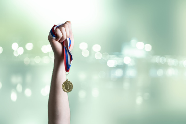 een persoon opgeheven hand winnen van de eerste plaats, hand vasthouden gouden medaille - Foto, afbeelding