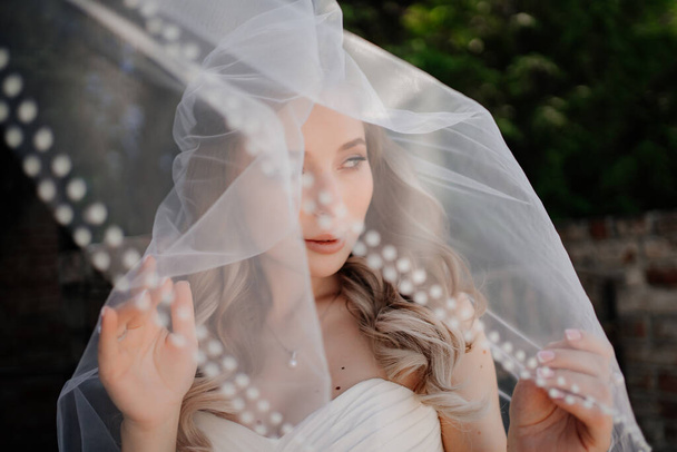 happy bride with long wavy hair under the veil outside. Wedding make-up.  - Fotoğraf, Görsel