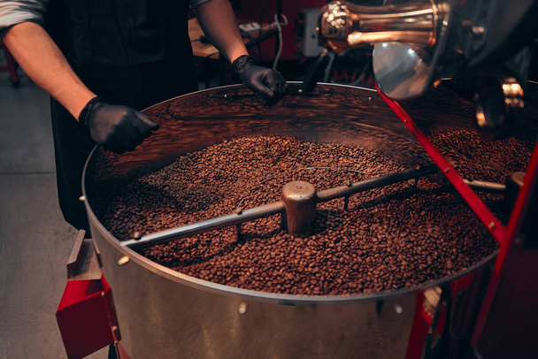 Imagen recortada de las manos de un hombre africano ocupado sintiendo los granos de café después de que solo se han tostado para realizar un control de calidad antes de que los granos se empaquetan y envían a nivel mundial. - Foto, Imagen