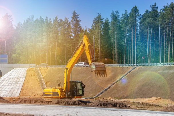 L'escavatore prepara il sito per la costruzione della strada. Macchine edili arancioni. Attrezzature pesanti movimento terra su lavori stradali - Foto, immagini