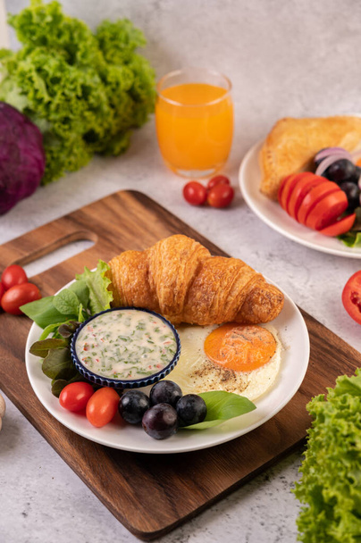 El desayuno consta de croissant, huevo frito, aderezo para ensaladas, uvas negras y tomates.. - Foto, imagen