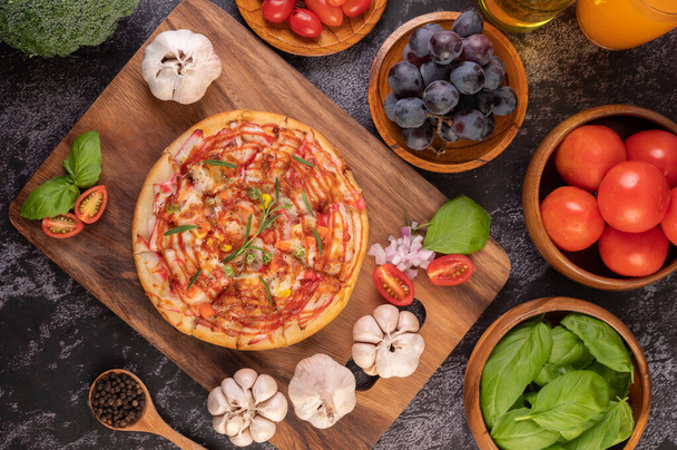 Pizza umieszczona na drewnianym talerzu z nasionami pieprzu. Pomidory i czosnek. Widok z góry. - Zdjęcie, obraz