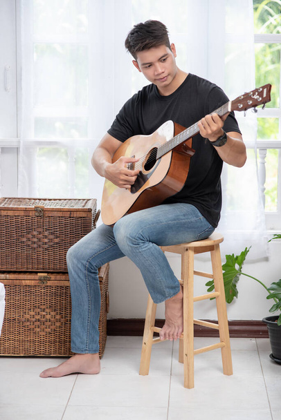 A man sitting and playing guitar on a chair - Fotó, kép