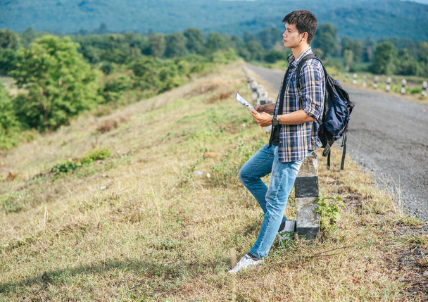 Άντρας ταξιδιώτης με σακίδιο Κρατώντας ένα χάρτη και στέκεται κοντά σε ένα χιλιόμετρο. - Φωτογραφία, εικόνα