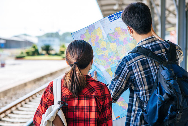 Male and female tourists look at the map beside the railway tracks. - Foto, Imagen