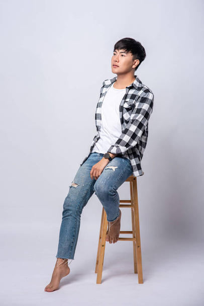 Ένας νεαρός με ριγέ πουκάμισο κάθεται σε μια ψηλή καρέκλα.. - Φωτογραφία, εικόνα