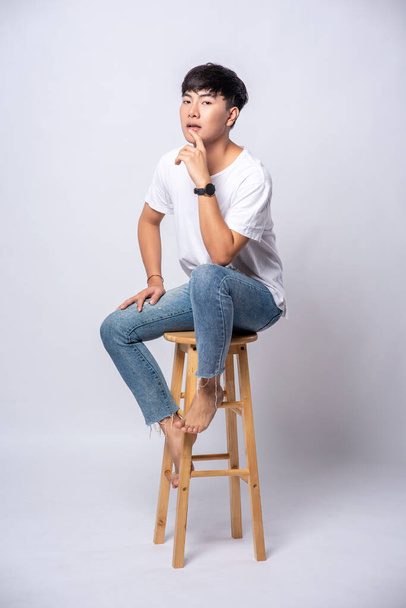 A young man in a white T-shirt is sitting on a high chair. - 写真・画像
