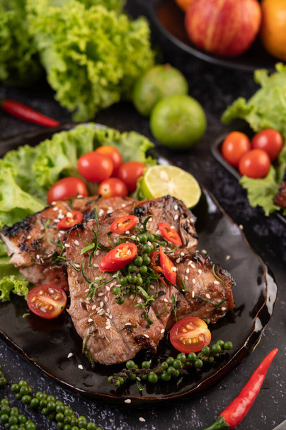 A Sliced pork steak topped with white sesame and fresh pepper seeds along with tomatoes, lemons, chili and lettuce. - Photo, Image