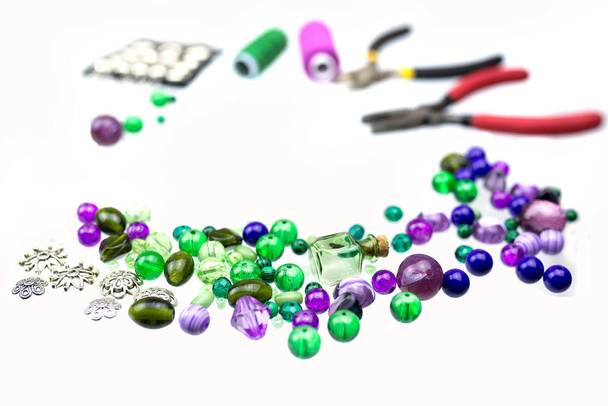 Rámeček, vyrobený ze zelených a fialových perlí, šicích nití a dalších dodavatelů šperků izolovaných na bílém pozadí. Selektivní soustředění. Zavřít. - Fotografie, Obrázek