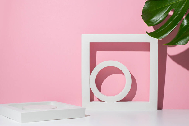 Λευκά γεωμετρικά podiums για παρουσίαση και φύλλα monstera σε λευκό ροζ φόντο. - Φωτογραφία, εικόνα