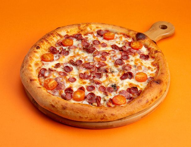 Pizza with sausages and tomatoes. On a yellow background. Selective focus - Photo, Image