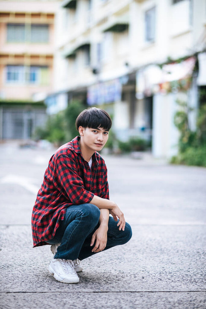Um jovem de camisa listrada sentado na rua. - Foto, Imagem