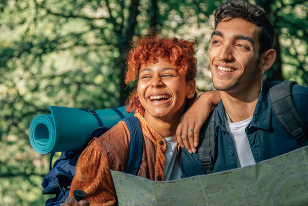 young multiethnic young couple on a backpacking trip looking at the map - Photo, Image