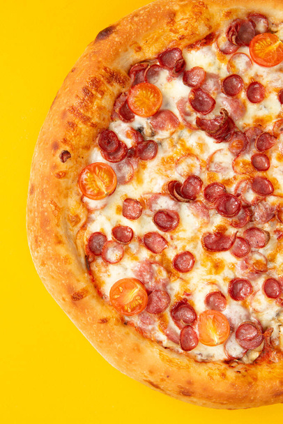 Pizza met worsten en tomaten. Op een gele achtergrond. Selectieve focus - Foto, afbeelding