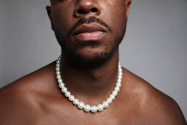 Cropped close-up of shirtless black man with pearl necklace over grey wall. - Фото, изображение