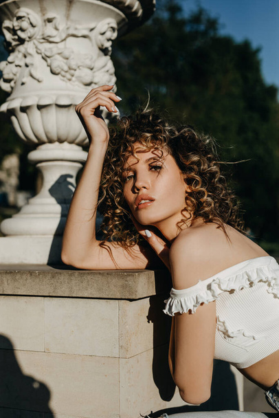 Young woman with curly hair posing outdoors next to a statue. - Photo, Image