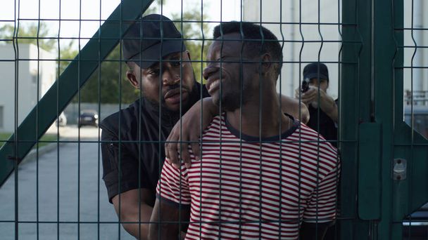 Politieagent ondervraagt zwarte gevangene in de buurt van grid - Foto, afbeelding