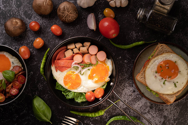 Ontbijt met gebakken eieren, worst en ham in een pan met tomaten. Chili en basilicum. - Foto, afbeelding