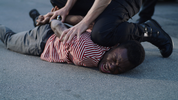 Полицейский надевает наручники на плачущего черного мужчину - Фото, изображение
