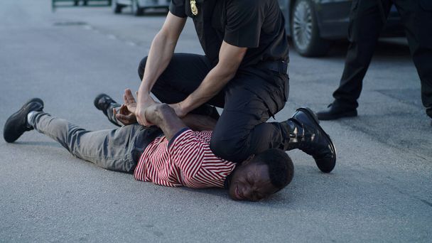 Policeman putting handcuffs on crying black man - Foto, afbeelding