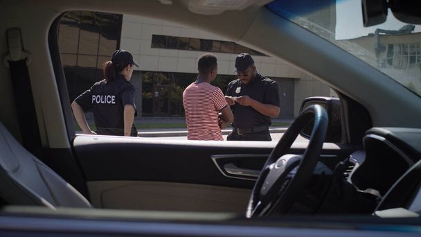 Monipuoliset poliisit tarkastamassa mustan kuljettajan asiakirjoja - Valokuva, kuva