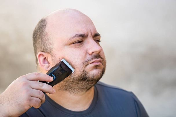 Rasage masculin ou coupe sa barbe à l'aide d'une tondeuse à cheveux ou d'un rasoir électrique - Photo, image